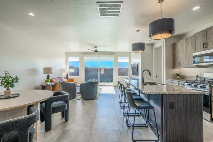 Kitchen with stainless steel appliances, a kitchen bar, light stone counters, an island with sink, and ceiling fan