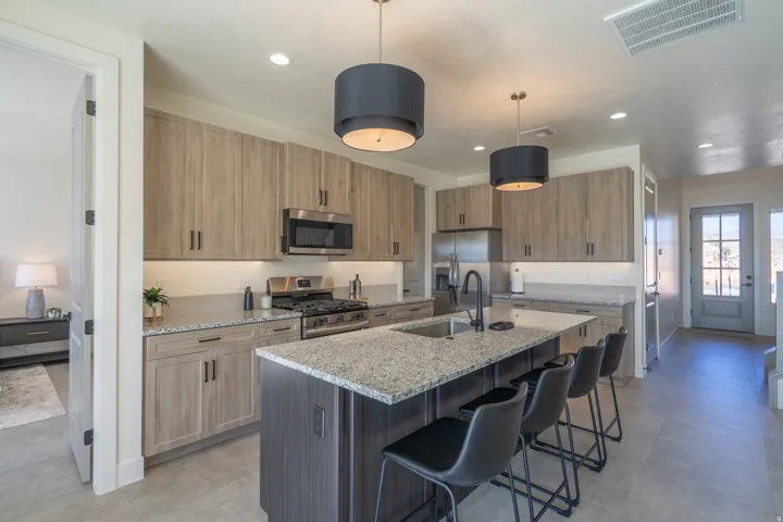 Kitchen with light stone countertops, stainless steel appliances, a kitchen breakfast bar, a center island with sink, and hanging light fixtures