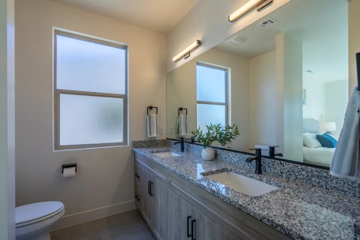 Full bath featuring double vanity, ensuite bathroom, dark tile patterned floors, and plenty of natural light
