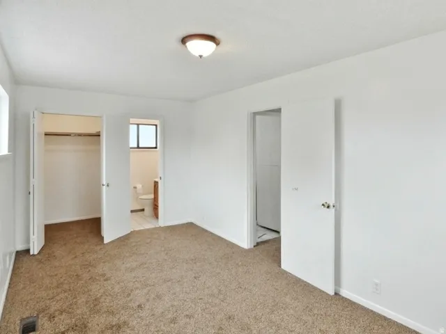 Unfurnished bedroom with a walk in closet, light carpet, and ensuite bath