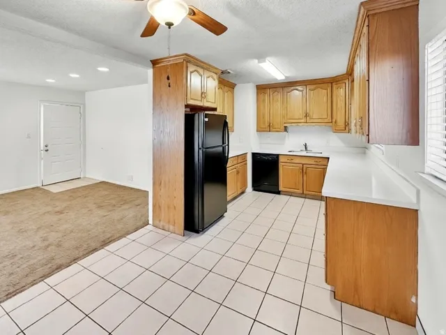 Kitchen featuring light colored carpet, light countertops, a textured ceiling, black appliances, and a ceiling fan