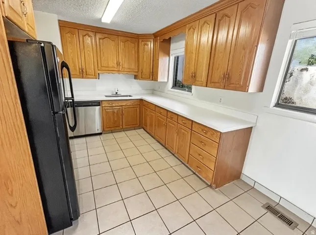 Kitchen featuring freestanding refrigerator, light countertops, dishwasher, wood finish cabinetry, and a textured ceiling