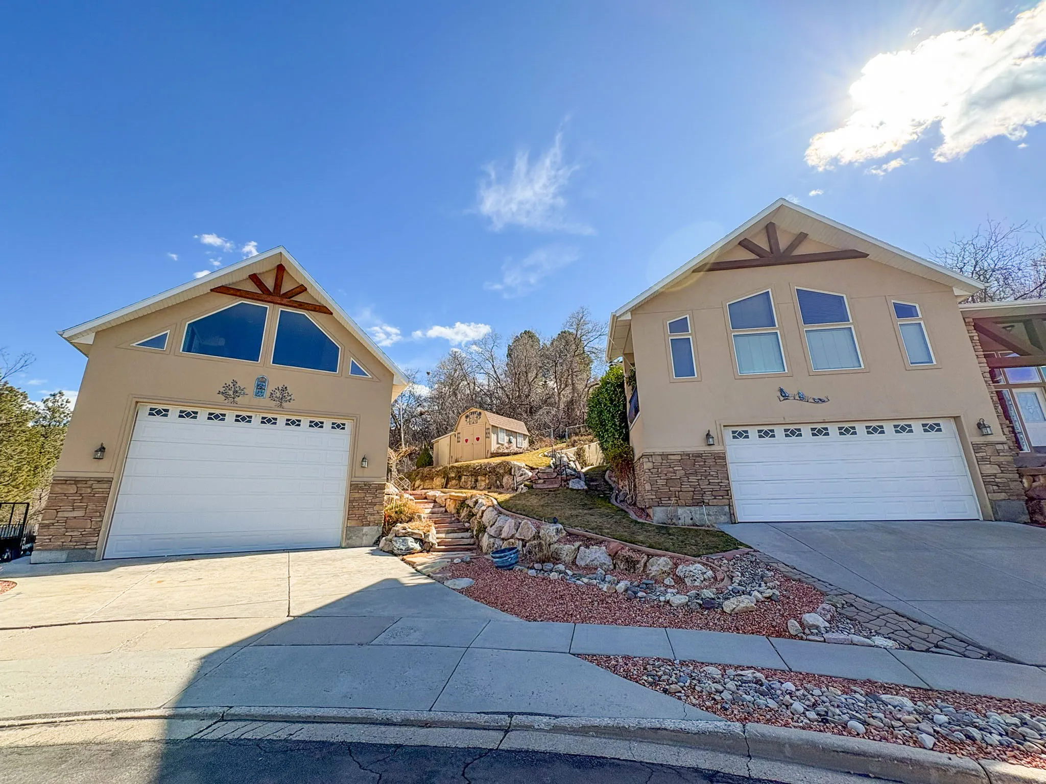 View of property exterior featuring stone siding, stucco siding, a garage, and driveway with detached garage with loft