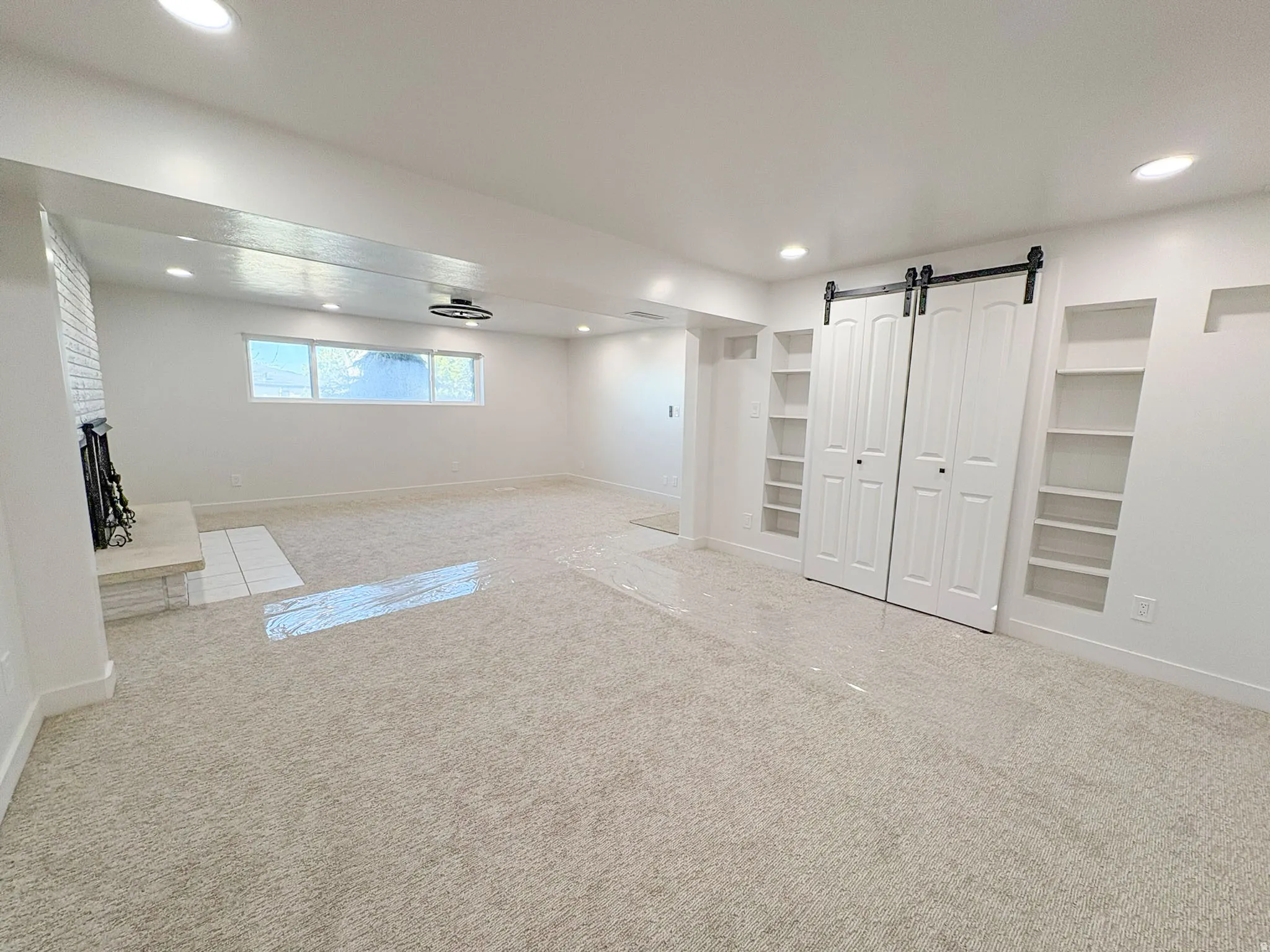 Basement with carpet, recessed lighting, built in features, a barn door, and a fireplace with raised hearth