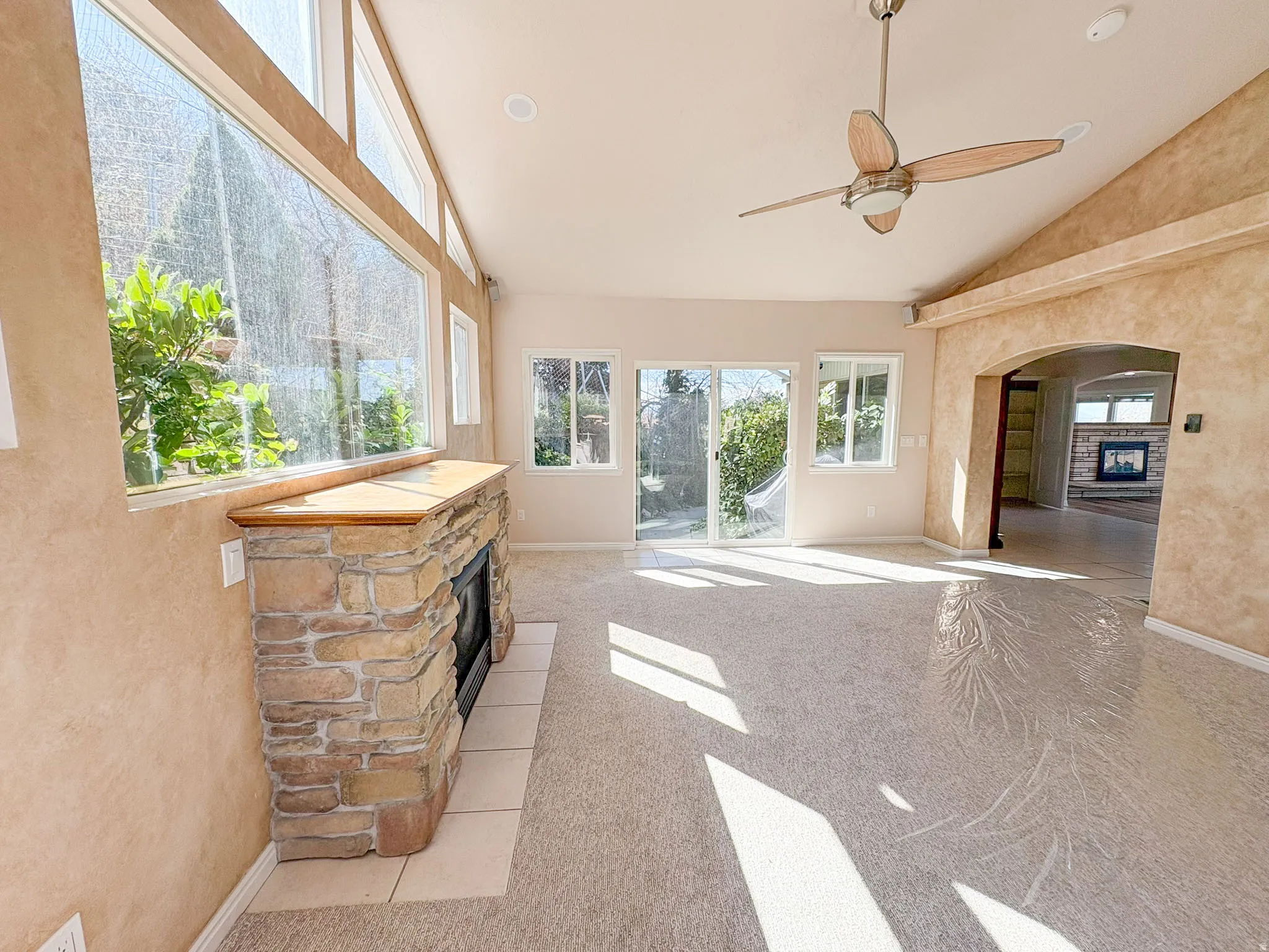 Sunroom with a fireplace, ceiling fan, lofted ceiling, light colored carpet, and arched walkways
