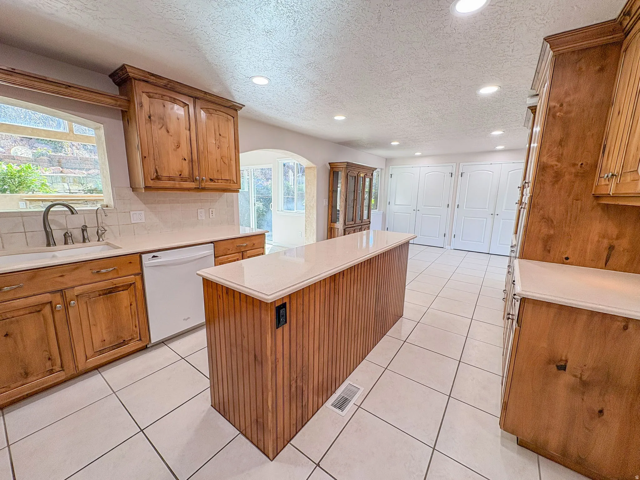Kitchen with wood finish cabinetry, a center island, a textured ceiling, arched walkways, and tasteful backsplash