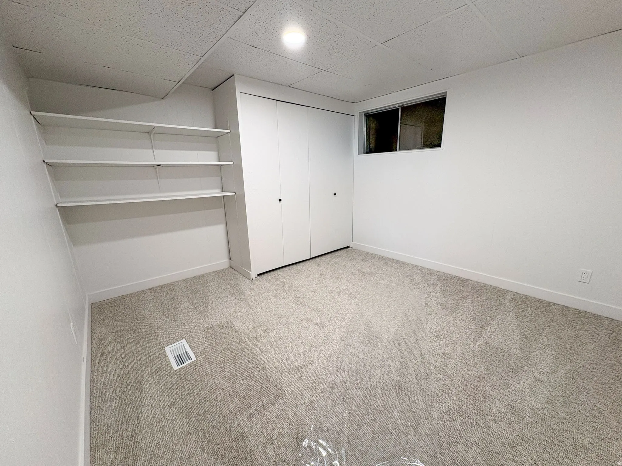 Unfurnished bedroom with a drop ceiling, light carpet, and a closet
