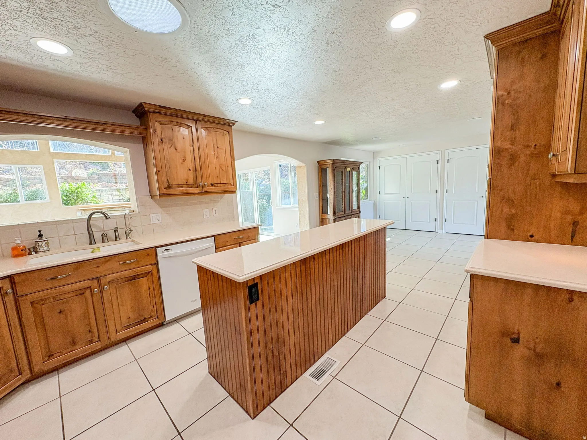 Kitchen with wood finish cabinets, a textured ceiling, a center island, decorative backsplash, and white dishwasher