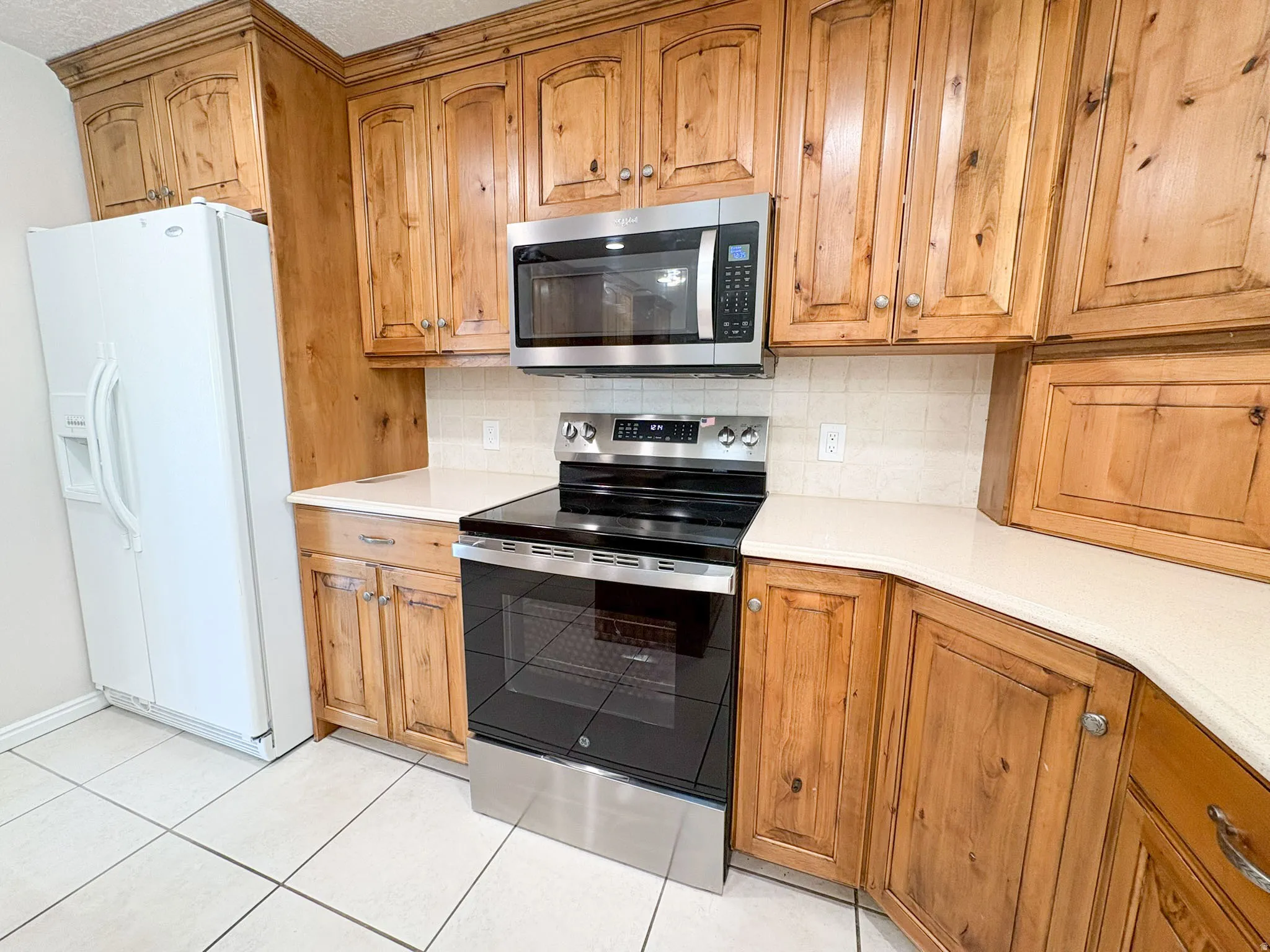 Kitchen featuring stainless steel appliances, tasteful backsplash, wood finish cabinets, and light tile patterned floors