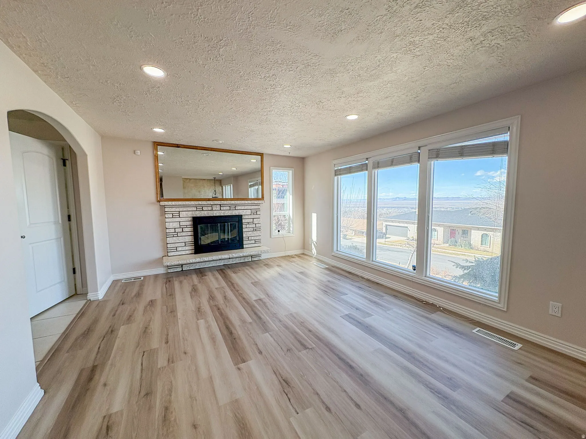 Unfurnished living room featuring recessed lighting, light wood-type flooring, a textured ceiling, arched walkways, and a stone fireplace