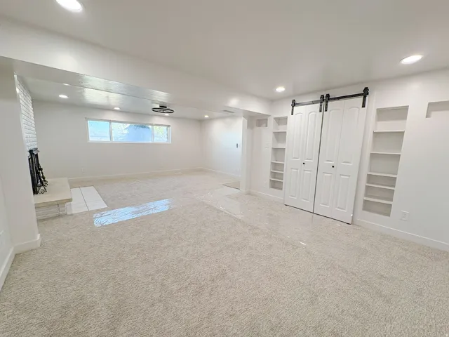 Basement with carpet, recessed lighting, built in features, a barn door, and a fireplace with raised hearth