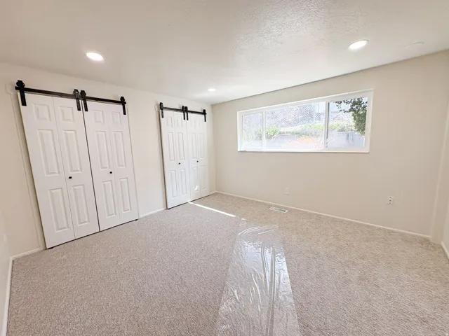 Unfurnished bedroom with a barn door, carpet floors, two closets, recessed lighting, and a textured ceiling