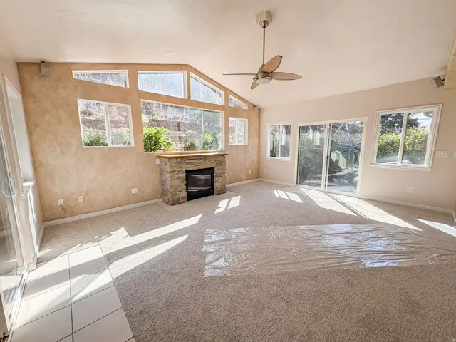 Unfurnished living room featuring light colored carpet, a stone fireplace, ceiling fan, and a high ceiling