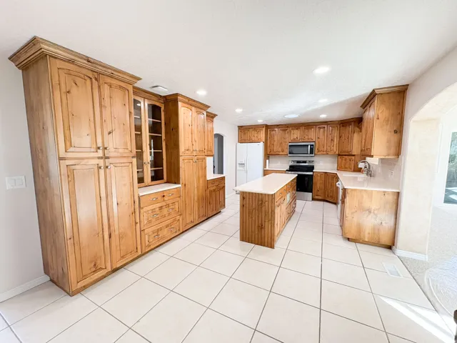 Kitchen featuring a kitchen island, arched walkways, stainless steel appliances, light tile patterned flooring, and light countertops