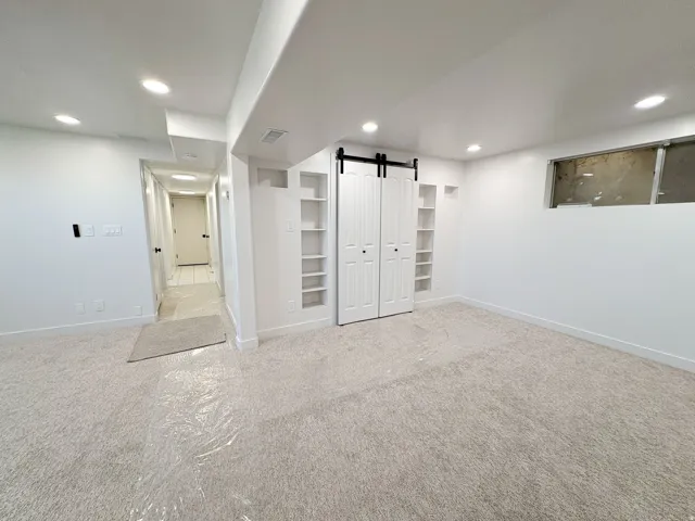 Finished great room/den area with a barn door, light colored carpet, and recessed lighting