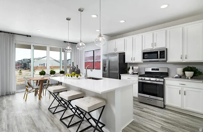 Kitchen featuring stainless steel appliances, white cabinetry, a kitchen bar, light wood finished floors, and an island with sink. Pictures are of a model home only! This home may feature different finishes than what is pictured.