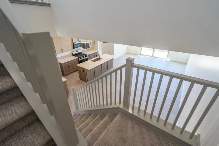 Carpeted staircase with white balusters overlooking an open-concept kitchen and living area featuring a central island, stainless steel appliances, and sliding glass doors