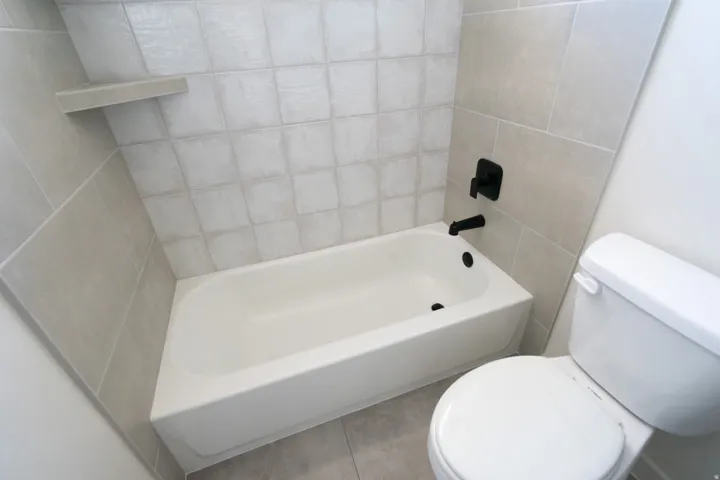 White bathtub with matte black fixtures, surrounded by light-toned square and rectangular tile