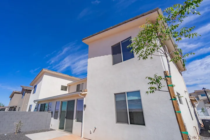 Stucco exterior featuring multiple windows and a young tree