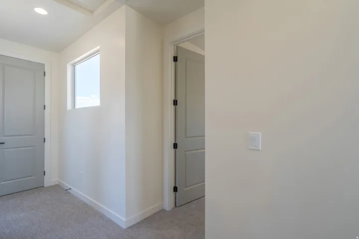 Interior hallway featuring light neutral wall paint, gray paneled doors with black hardware, a high-set rectangular window, recessed ceiling lighting, and gray carpet flooring
