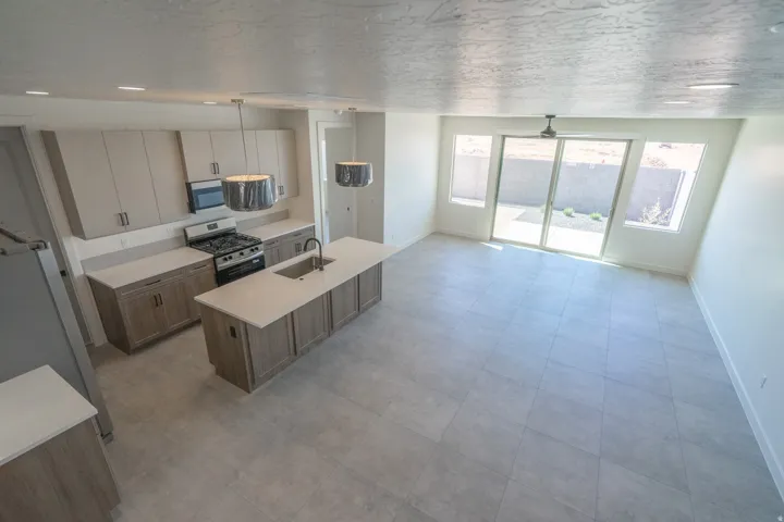 Spacious kitchen and living area featuring an island with sink, stainless steel appliances, modern pendant lighting, and large format tile flooring