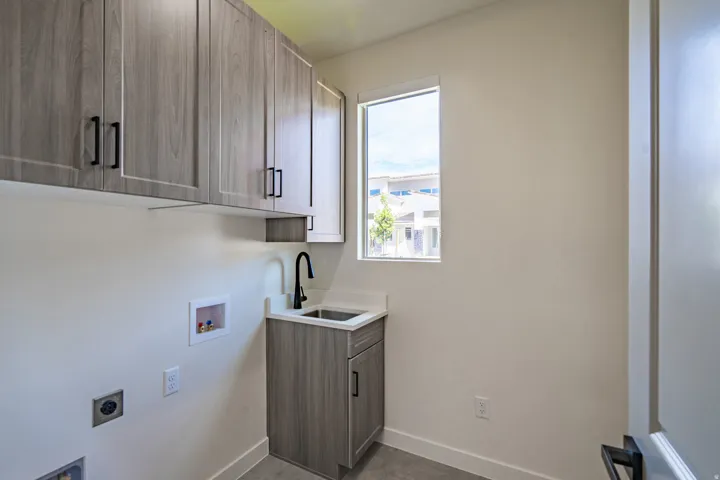 Utility room featuring wood-finish cabinetry with matte black hardware, a built-in sink with a matte black faucet, and a window providing natural illumination