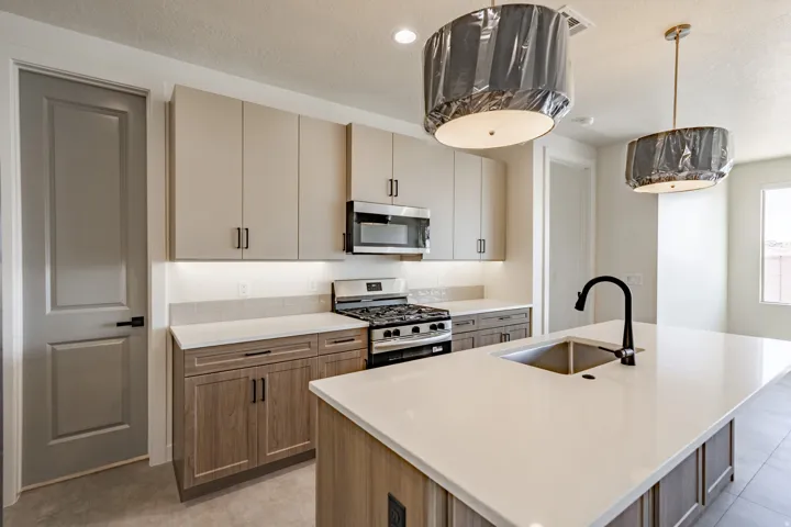 Kitchen featuring a large island with an undermount sink and matte black faucet, stainless steel appliances, two-tone cabinetry, under-cabinet lighting, and tile flooring