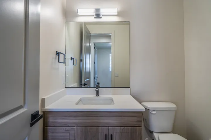 Bathroom vanity featuring a light wood-finish cabinet with dark hardware, a white countertop, and an integrated rectangular sink