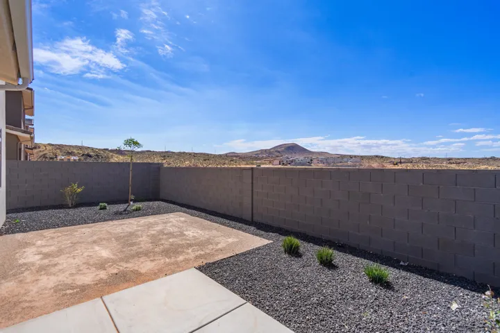 Expansive backyard featuring a concrete patio, dark gravel ground cover, and a retaining wall