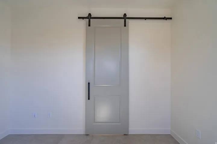 Gray paneled barn door with black hardware, set against light neutral walls and white baseboards