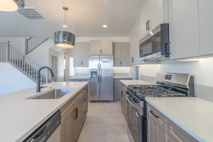 Gourmet kitchen featuring a peninsula island with an undermount sink, stainless steel appliances, light-toned cabinetry, solid surface countertops, and recessed lighting