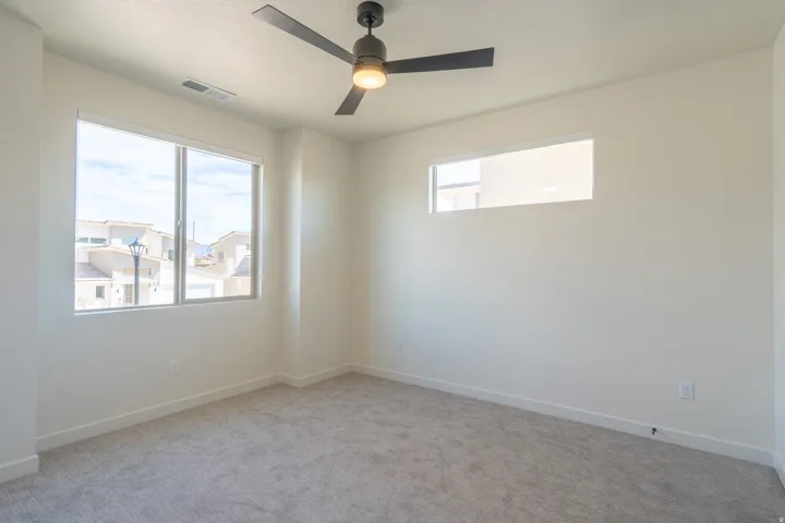 Carpeted room featuring a ceiling fan with integrated lighting, two distinct windows, and light-toned walls