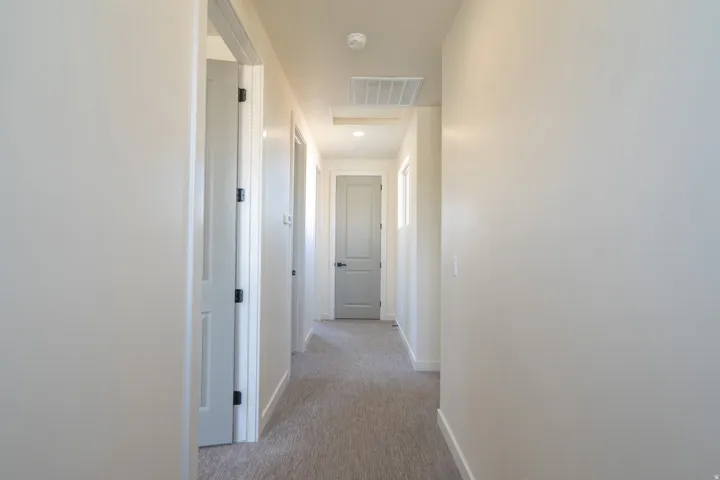 Hallway featuring light neutral wall paint, gray carpet flooring, recessed lighting, and multiple interior doors with dark hardware