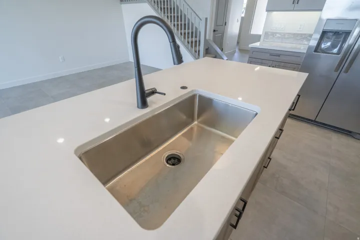 Kitchen island featuring a stainless steel undermount sink, a matte black gooseneck faucet, light-toned countertops, and dark cabinet hardware