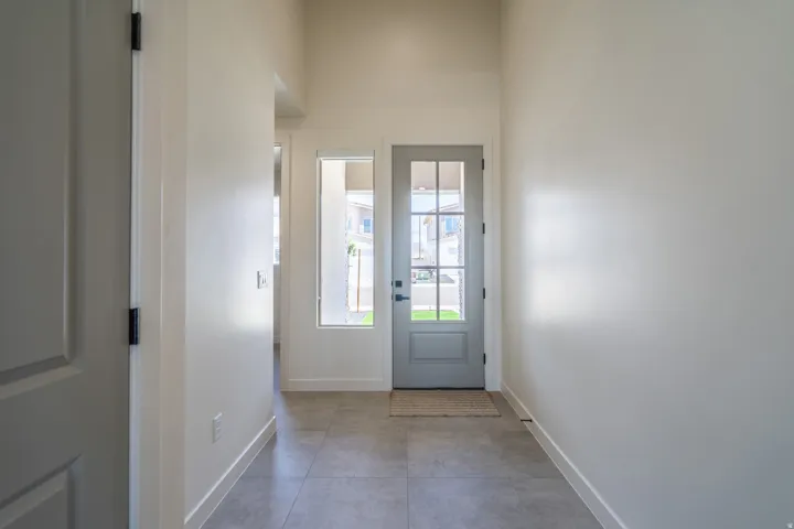 Entryway featuring a grey paneled door with multiple glass lites, a sidelite window, light grey tile flooring, and high ceilings