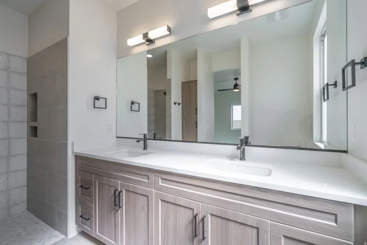 Bathroom vanity featuring a dual sink, white countertop, and light wood-finish cabinetry with dark hardware