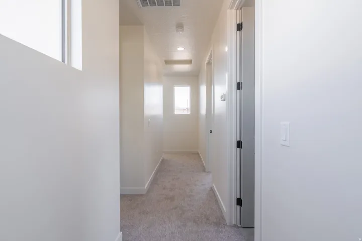 Hallway with neutral tone carpeting and crisp white walls