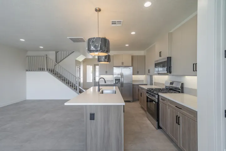 Modern kitchen featuring an island with an undermount sink and matte black faucet, stainless steel appliances, light wood-finish lower cabinetry, and light gray upper cabinetry