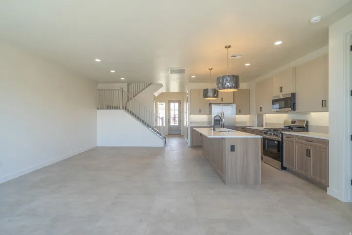 Open-concept kitchen featuring an oversized island with an undermount sink, stainless steel appliances, two-tone cabinetry, and pendant lighting