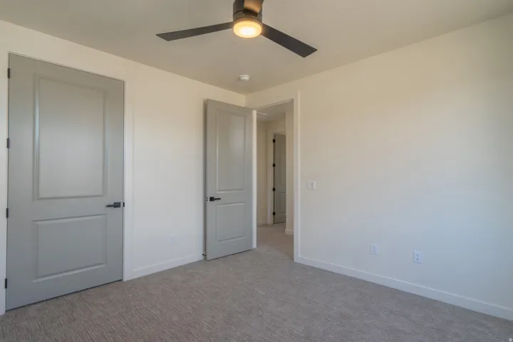 Room featuring light-toned walls, textured gray carpeting, and a dark-toned ceiling fan with integrated lighting