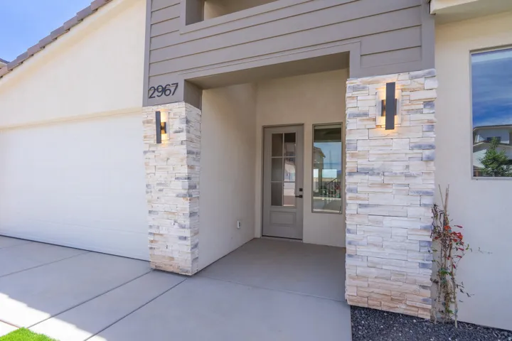 Modern exterior featuring a stacked stone column, contemporary outdoor lighting, a paneled front door with glass inserts, an attached garage, and a concrete driveway