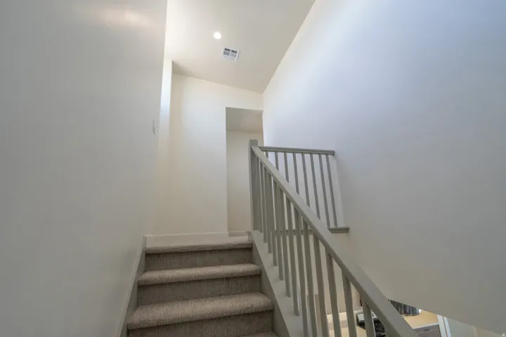 Carpeted staircase featuring a light gray balustrade and handrail, recessed ceiling lighting, and a square ceiling vent