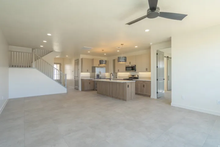 Open-concept living space featuring light-toned tile flooring, a contemporary kitchen, and a staircase with a light wood balustrade