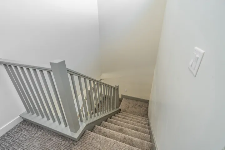 Staircase featuring light gray balusters, a matching handrail, and carpeted treads