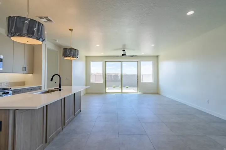 Open-concept kitchen and living area featuring a large center island with integrated sink, light wood-finish cabinetry, stainless steel appliances, and sleek tile flooring throughout