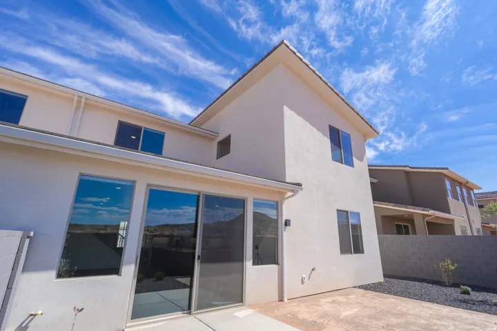 Rear exterior featuring a sliding glass door, multiple windows, and a concrete patio