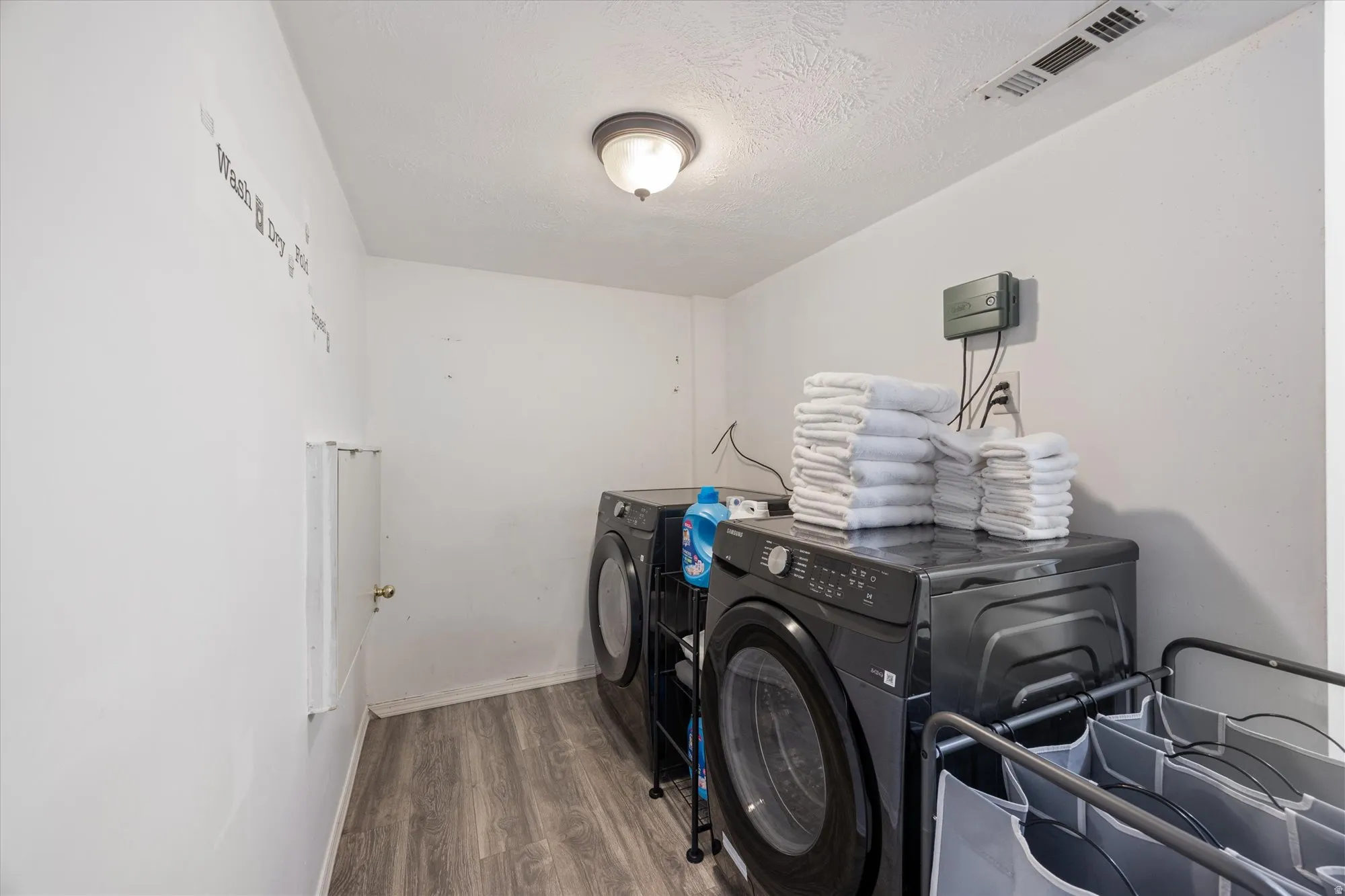 Laundry area with wood finished floors, washing machine and dryer, and a textured ceiling
