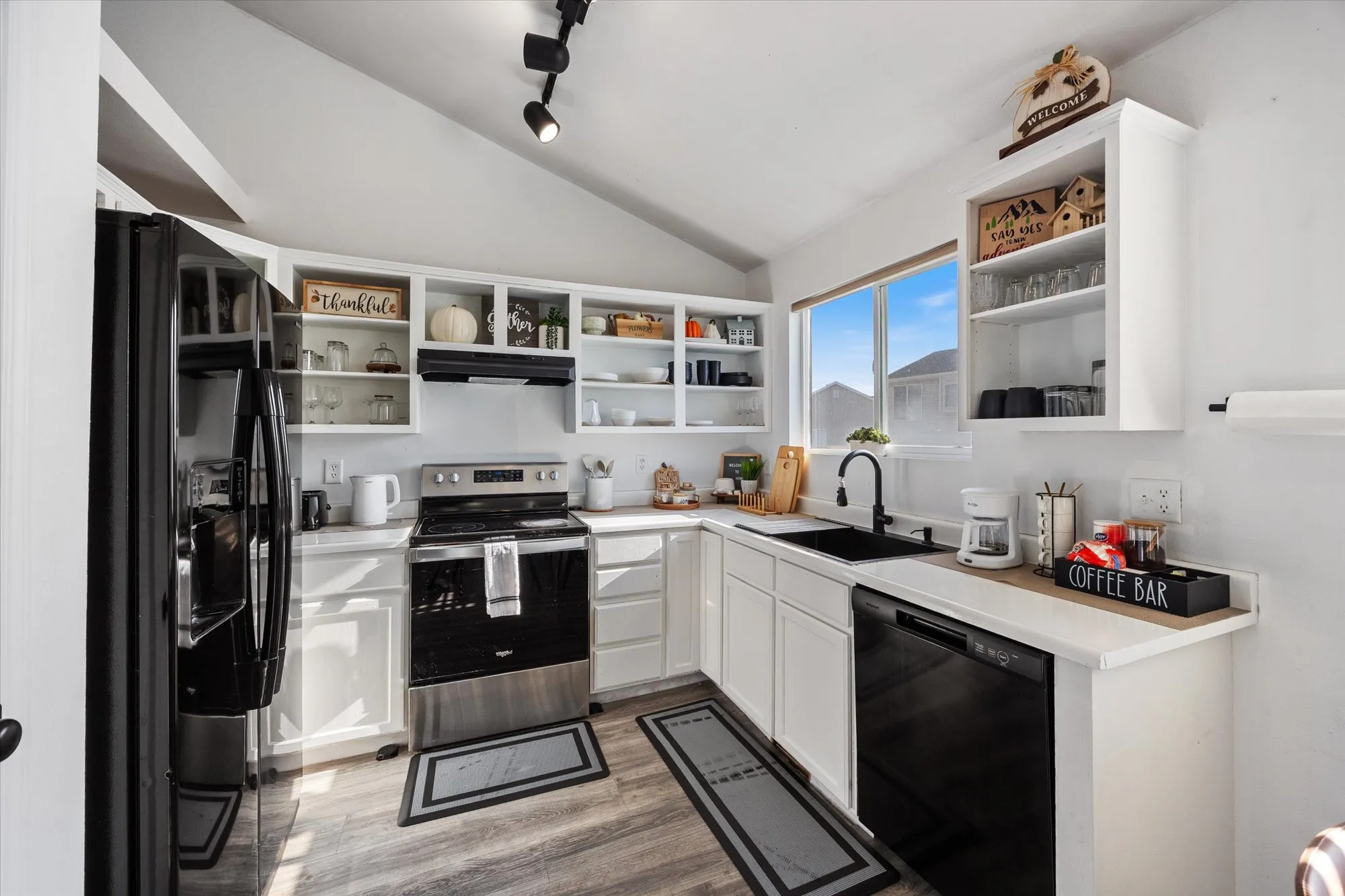 Kitchen featuring white cabinets, black appliances, light countertops, vaulted ceiling, and open shelves
