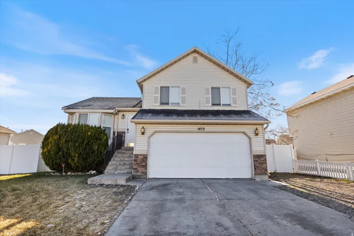 Tri-level home featuring driveway, an attached garage, and stone siding