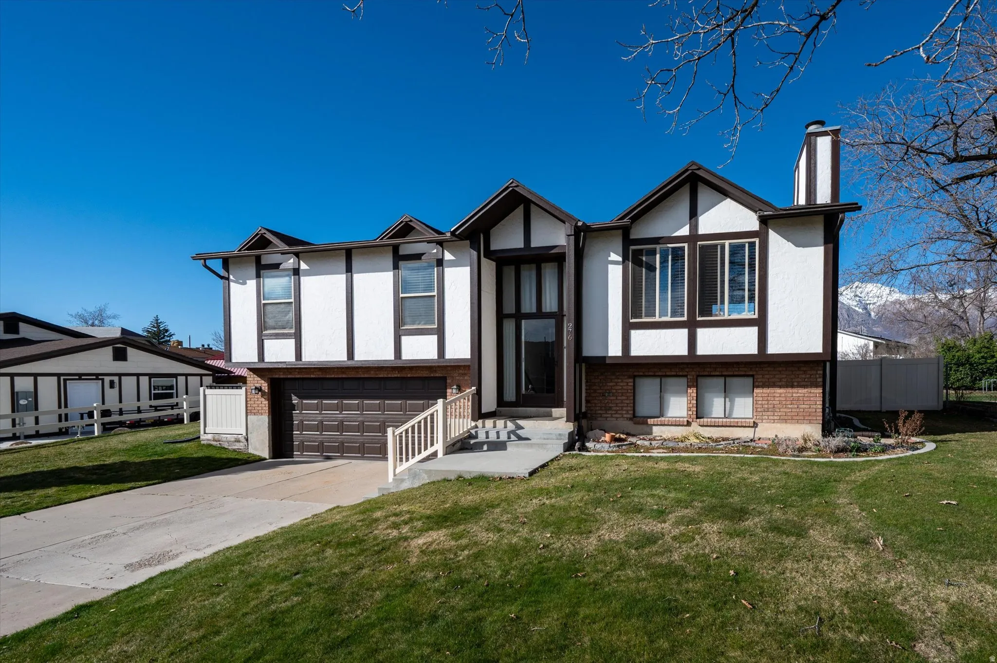 View of front of home with stucco siding, brick siding, a chimney, and driveway